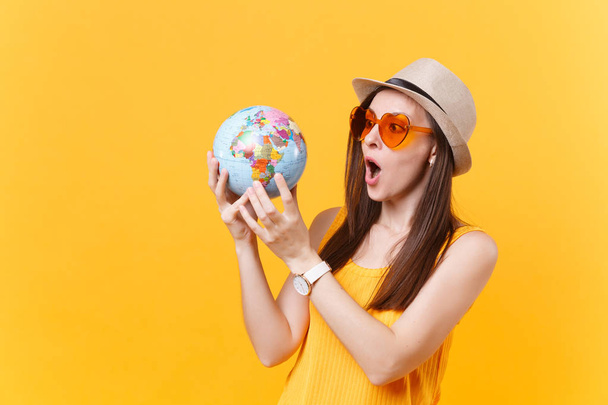 Retrato de mujer turista en sombrero de verano, gafas naranjas sostienen en las manos globo aislado sobre fondo amarillo. Viajar al extranjero para viajar fin de semana escapada. Concepto de viaje aéreo. Detener basura de la naturaleza
 - Foto, imagen