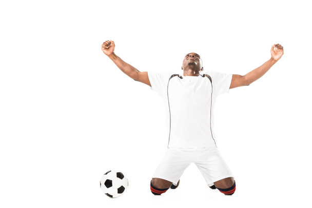 triumphing young african american soccer player kneeling near ball isolated on white  - Fotoğraf, Görsel