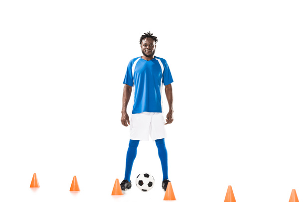 smiling young african american soccer player training with ball and marker cones isolated on white  - Photo, Image