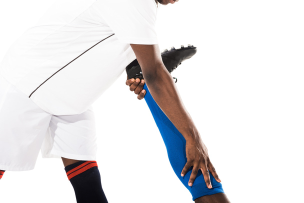 cropped shot of young african american sportsman stretching leg of soccer player isolated on white - 写真・画像
