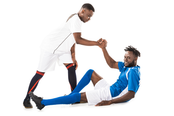 young african american sportsman helping soccer player lying isolated on white - Photo, Image