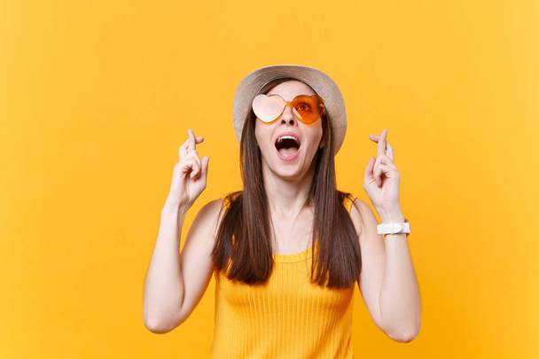Waiting for special moment. Portrait of smiling happy woman in orange glasses keeping fingers crossed. Making wish. Copy space isolated on yellow background. People sincere emotions lifestyle concept - Photo, image