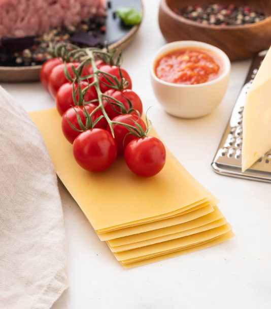 Ingredients for Italian lasagna with fresh cherry tomatoes and green basil leaves on sheets of dried pasta. Copy space. - Φωτογραφία, εικόνα