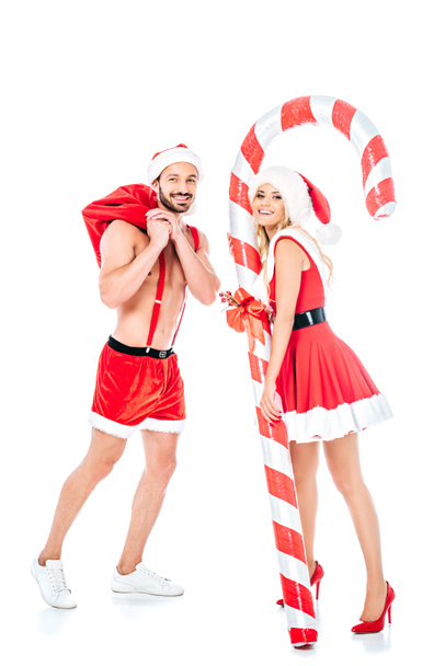 attractive young woman with striped christmas stick and muscular shirtless man in santa hat isolated on white background - 写真・画像