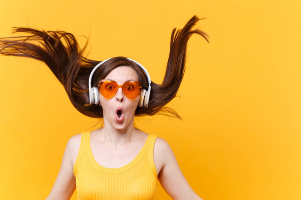Προσωπογραφία ενθουσιασμένος χαρούμενα γέλια αστείο κόμικ σε πορτοκαλί γυαλιά στα ακουστικά με φτερουγίσματα μαλλιά που απομονώνονται σε κίτρινο φόντο. Άνθρωποι ειλικρινή συναισθήματα έννοια τρόπου ζωής. Περιοχή διαφήμισης - Φωτογραφία, εικόνα