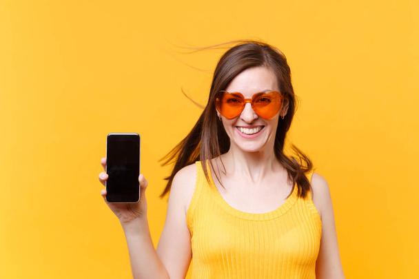 Muotokuva innoissaan iloinen nauru hauska sarjakuva nainen oranssi lasit lepattavat hiukset pidä matkapuhelin tyhjä näyttö kopioi tilaa eristetty keltaisella taustalla. Mainosalue
 - Valokuva, kuva