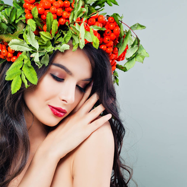 Mignon visage féminin. Jeune femme avec longue coiffure ondulée, maquillage et baies rouges et couronne de feuilles de reen
 - Photo, image