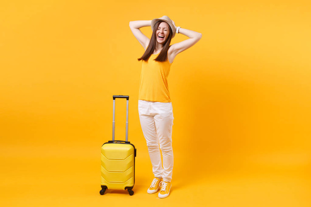Traveler tourist woman in summer casual clothes, hat with suitcase isolated on yellow orange background. Female passenger traveling abroad to travel on weekends getaway. Air flight journey concept - Photo, image