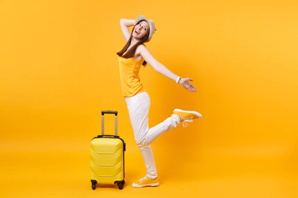 旅行観光女性夏カジュアルな服を着て、黄色オレンジ色の背景に分離されたスーツケースと帽子。女性の乗客は、週末の息抜きに旅行に海外旅行します。空気飛行の旅のコンセプト - 写真・画像