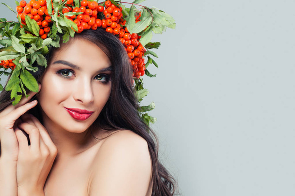 Smiling woman with makeup, long wavy hairstyle and red berries and green leaves on background with copy space - Photo, Image