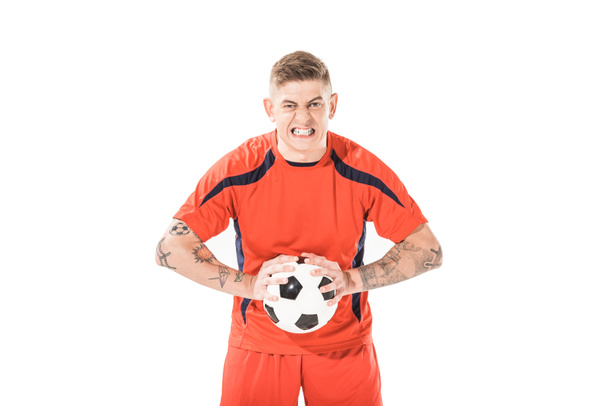 jovem jogador de futebol irritado segurando bola e olhando para a câmera isolada no branco
 - Foto, Imagem