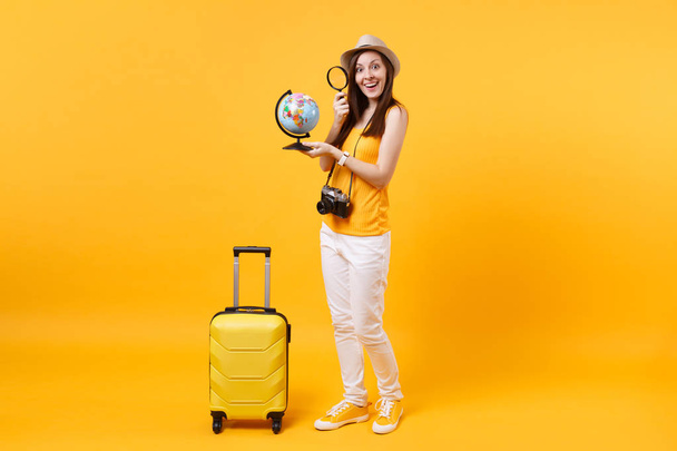 Matkailija turisti nainen kesällä rento vaatteita, hattu maapallo, matkalaukku eristetty keltainen oranssi tausta. Matkustaja matkustaa ulkomaille viikonloppuisin lomalle. Lentomatkan käsite
 - Valokuva, kuva