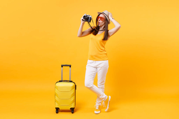 Tourist woman in summer casual clothes with suitcase, retro vintage photo camera isolated on yellow orange background. Passenger traveling abroad to travel on weekends getaway. Air flight concept - Photo, Image