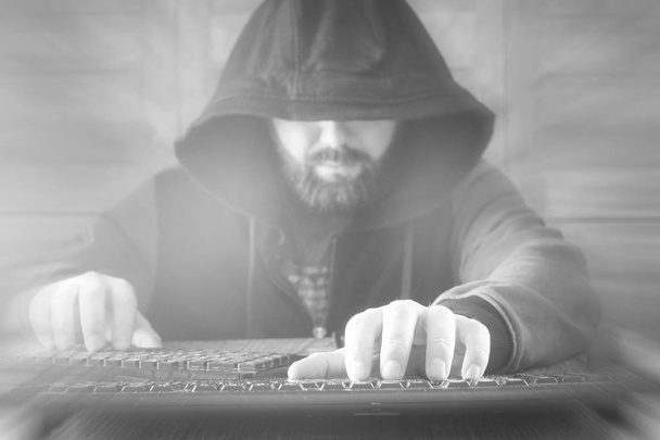 De hacker in de kap zit en werkt achter de computer - Foto, afbeelding