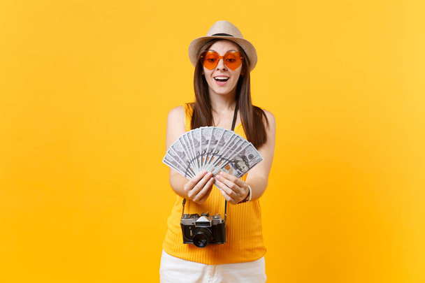 Turistické žena v létě ležérní oblečení, čepice drží svazek spoustu dolarů, hotovost, samostatný na žlutém pozadí. Žena cestování o víkendech útočiště na cestách do zahraničí. Koncept letu vzduchem - Fotografie, Obrázek