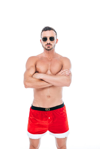 serious muscular man in christmas shorts and sunglasses standing with crossed arms isolated on white background  - Foto, imagen