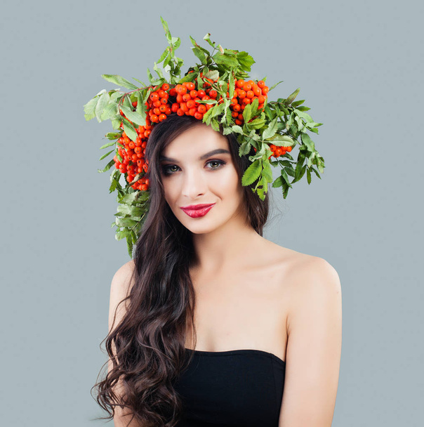 Smiling brunette woman fashion model with healthy curly hair, makeup and red berries and green leaves, portrait - Foto, Imagem