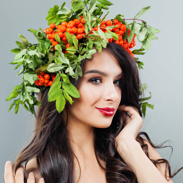 Makyaj, dalgalı saç ve kırmızı meyveler ve başındaki yeşil yaprakları olan mutlu kadın portresi - Fotoğraf, Görsel