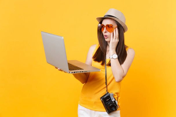 Surullinen järkyttynyt turisti nainen kesällä rento vaatteita, hattu tilalla kannettavan tietokoneen eristetty keltainen oranssi tausta. Tyttö matkustaa ulkomaille viikonloppumatkalle. Lentomatkan käsite
 - Valokuva, kuva