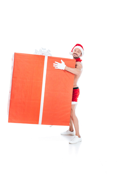 shirtless muscular man in christmas hat holding big gift box isolated on white background - Photo, Image