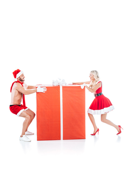side view of happy couple in christmas clothes pulling big gift box in different directions isolated on white background  - Photo, Image