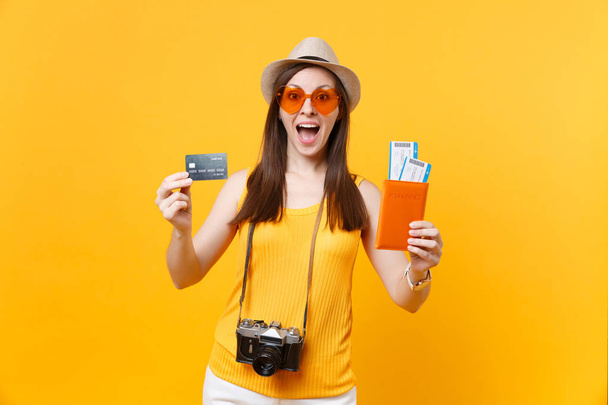 Mujer turista feliz en ropa casual de verano, sombrero con tarjeta de crédito, pasaportes aislados sobre fondo amarillo anaranjado. Mujer viajando al extranjero para viajar los fines de semana de escapada. Concepto de vuelo aéreo
 - Foto, imagen