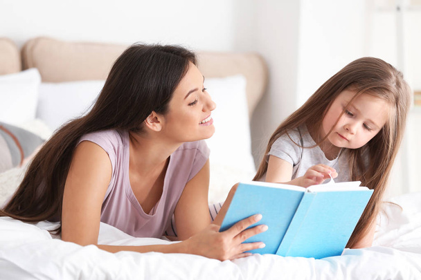 Mother and her daughter reading book together at home - Фото, изображение