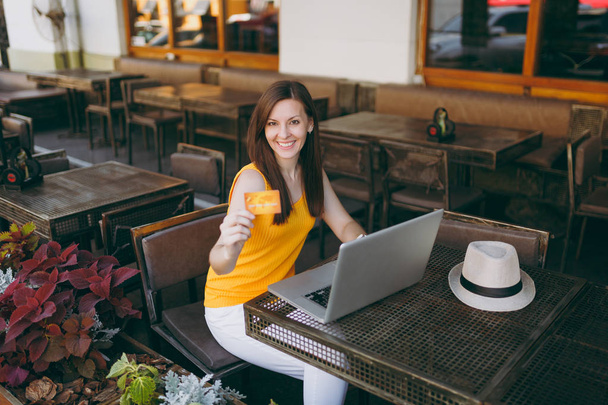 Woman in outdoors street coffee shop cafe sitting at table with modern laptop pc computer, hold in hand credit card. Mobile Office in restaurant in free time. Lifestyle freelance business concept - Foto, Imagem