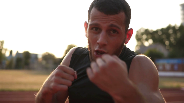 Accelerated handhelded footage of a young boxer exercising outdoors. Portrait of a man boxing with invisible opponent, punching. Front view - Filmati, video