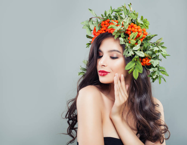 Smiling woman on background with copy space. Brunette model with long wavy hair, makeup and autumn berries and leaves - Фото, изображение