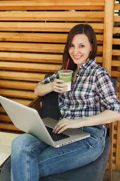 Kadın rahat kıyafetler içinde oturan, modern dizüstü pc bilgisayar üzerinde çalışma, serbest zaman sırasında rahatlatıcı açık havada sokak yaz kahve dükkanı ahşap Cafe. Mobil ofis. Yaşam tarzı serbest iş kavramı - Fotoğraf, Görsel