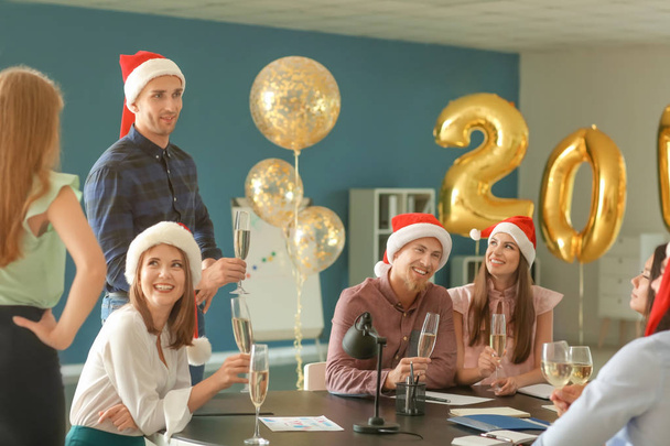 Молодые люди с бокалами шампанского празднуют Рождество на корпоративной вечеринке в офисе
 - Фото, изображение