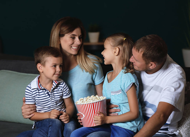 Szczęśliwa rodzina jedzenie popcorn podczas oglądania telewizji w godzinach wieczornych - Zdjęcie, obraz