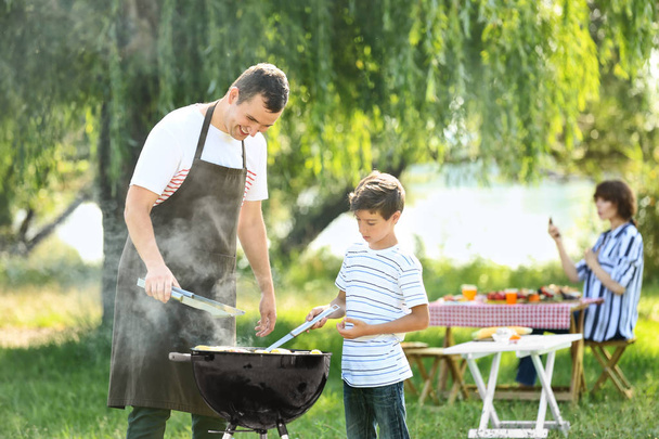 Pieni poika isänsä kanssa kokkaamassa maukasta ruokaa grillillä ulkona
 - Valokuva, kuva