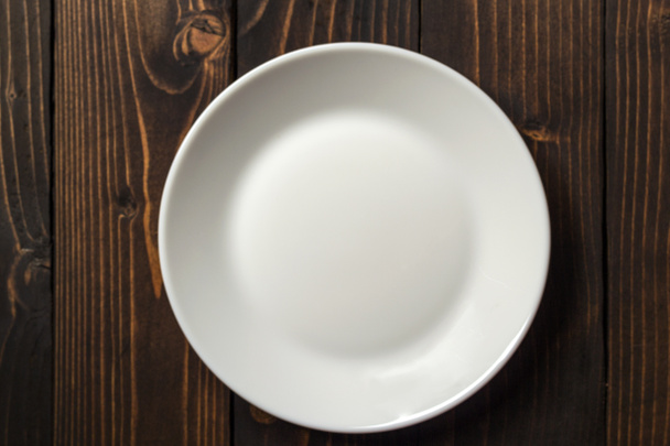 Λευκό στρογγυλό πιάτο σε ένα σκοτεινό ξύλινο τραπέζι. Θέα από ψηλά. - Φωτογραφία, εικόνα