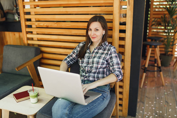 Vrouw in openlucht straat coffeeshop houten zomerterras zitten in casual kleding, werken op moderne laptop PC, ontspannen tijdens de vrije tijd. Mobiel kantoor. Levensstijl freelance bedrijfsconcept - Foto, afbeelding