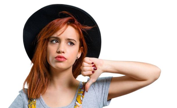 Cool redhead girl with hat showing thumb down sign with negative expression - 写真・画像