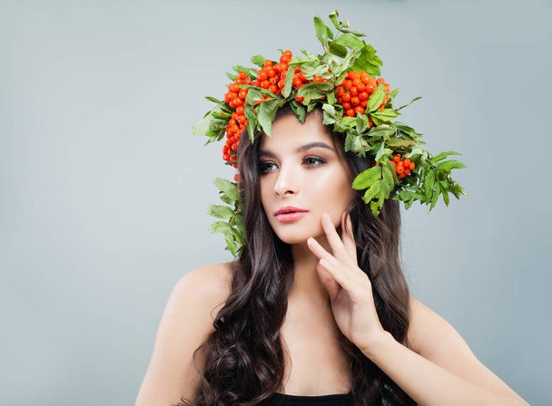 Sexy brunette woman fashion model in wreath of red berries and green leaves, portrait - Фото, изображение