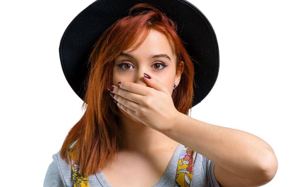 Cool roodharige meisje met hoed die betrekking hebben op mond met handen - Foto, afbeelding