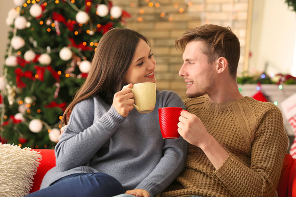 Χαριτωμένο νεαρό ζευγάρι πίνοντας ζεστή σοκολάτα στο σπίτι την παραμονή των Χριστουγέννων - Φωτογραφία, εικόνα