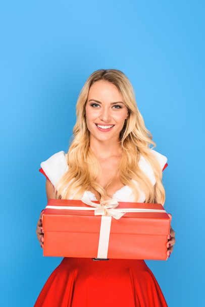smiling young woman in christmas dress holding gift box isolated on blue background - Фото, зображення