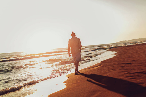 Un uomo che cammina sulla spiaggia al tramonto
. - Foto, immagini