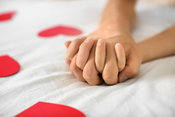 Młoda para z czerwone serca, trzymając się za ręce leżąc na łóżku w domu - Zdjęcie, obraz