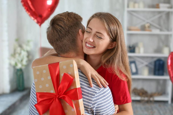 junges Paar mit Geschenkbox umarmt sich zu Hause - Foto, Bild