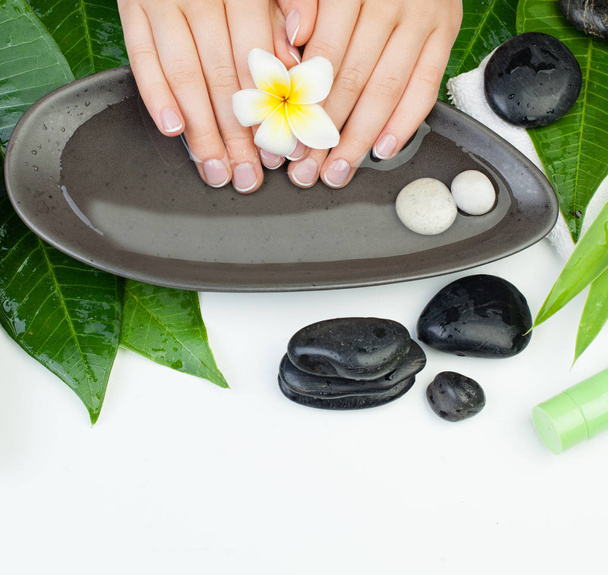 Beautiful female hands in bowl of water with flowers, stones, towel and cream tubes - Photo, Image