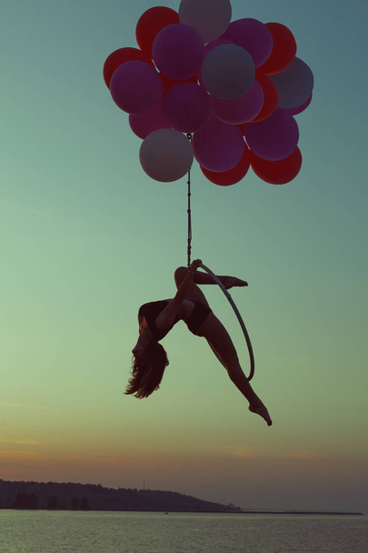 Girl gymnast sits on an acrobatic ring. Ring holding balloons. - Photo, Image