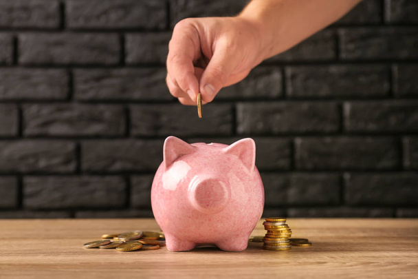 Woman putting coin into piggy bank on table - Photo, Image
