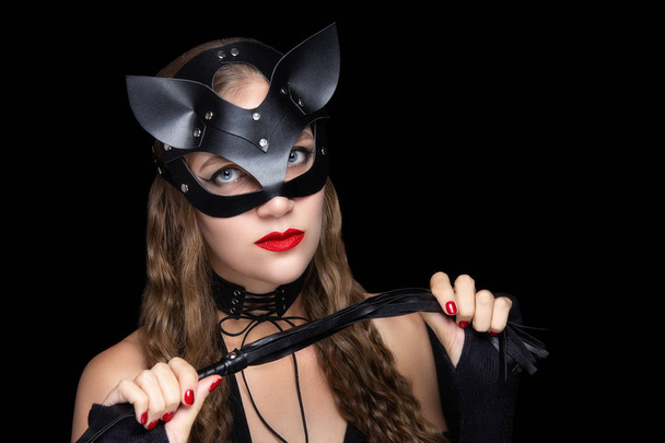 Woman wearing cat mask, sexual roleplay. Professional make-up bright red lipstick. Subordinate and dominate partner. Ready to Halloween party kitten killer assassin. Holds a whip in her hand to pump - Foto, Imagen