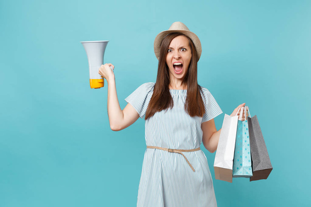 Portrait woman in summer dress, hat holding packages bags with purchases after shopping, scream in megaphone, announces discounts sale isolated on blue pastel background. Copy space for advertisement - Foto, Bild
