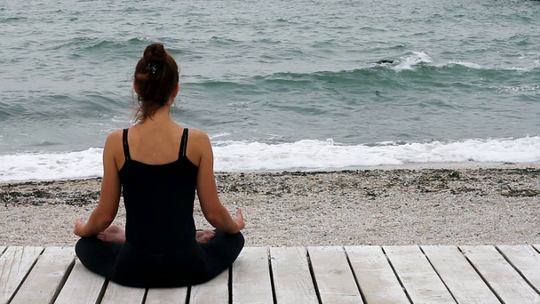 Girll κάθεται μέσα στη σιωπή σε θέση lotus και διαλογισμό δίπλα στη θάλασσα - Πλάνα, βίντεο